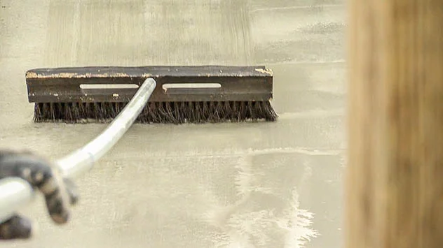 Stiff-bristled brush dragging over a concrete floor.